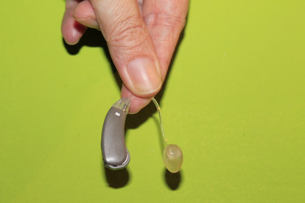 How To Get Used To Your Hearing Aids. Hearing device hend in hand with the citrus green backgound
