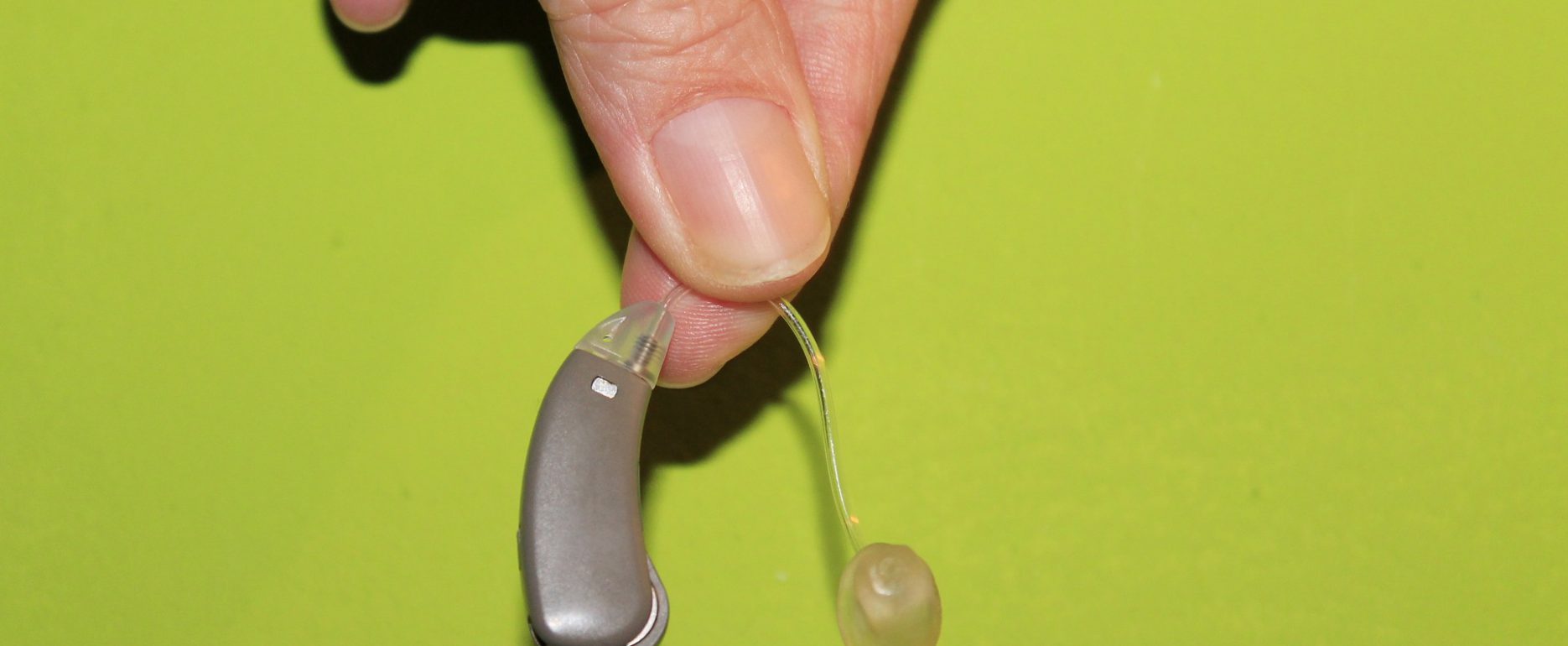 How To Get Used To Your Hearing Aids. Hearing device hend in hand with the citrus green backgound