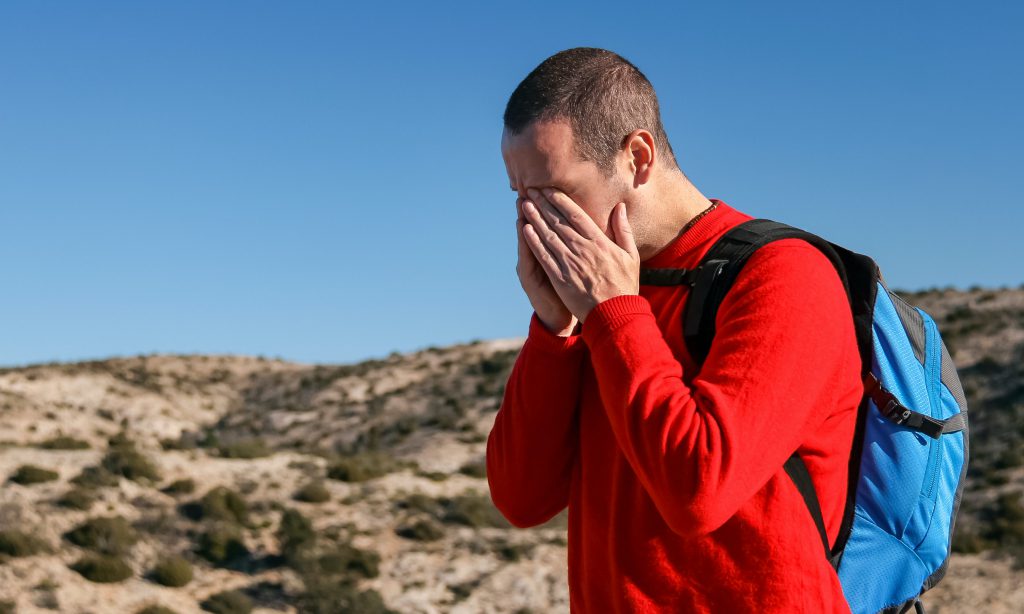 Man hiking in a red shirt having a headache